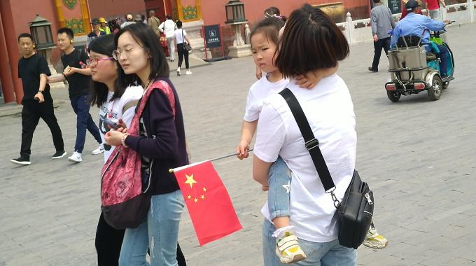 Äiti kantaa tyttöä, jolla on kädessään Kiinan lippu.