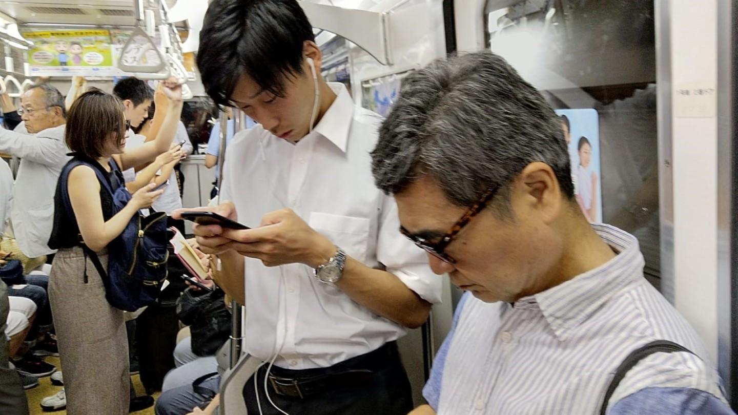 Japanilaiset miehet selaavat kännyköitä täydessä metrossa.