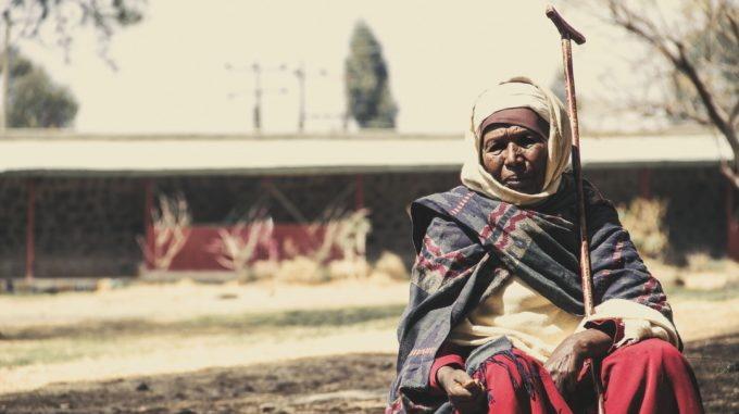 Vanha etiopialainen nainen istuu talon edustalla.