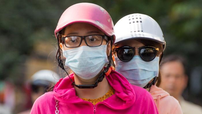 Aasialaiset naiset mopon kyydissä maskit kasvoilla.
