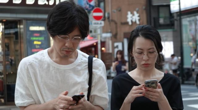 Japanilainen mies ja nainen käyttävät kännykköitään.