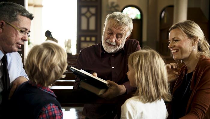 Eri-ikäisiä ihmisiä tutkimassa Raamattua kirkossa.