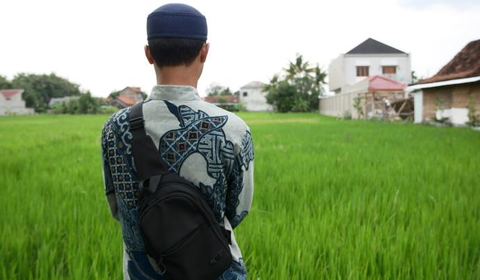 Indonesialainen mies katselee pellonreunalla.