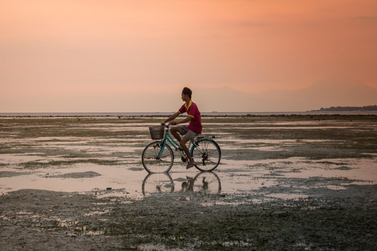 Poika ajaa polkupyörää auringonlaskun aikaan.