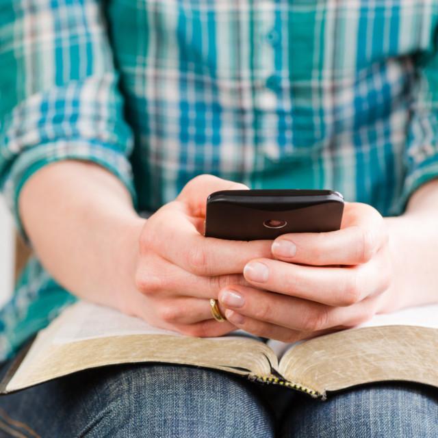 Nainen istuu kännykkä kädessä ja Raamattu sylissä auki.