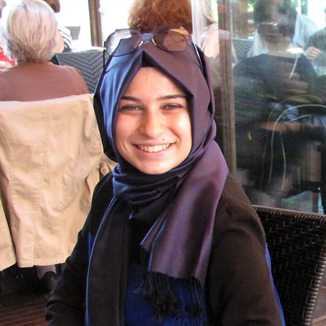 Hymyilevä turkkilainen nainen, jolla on huivi päässä ja aurinkolasit otsalla.