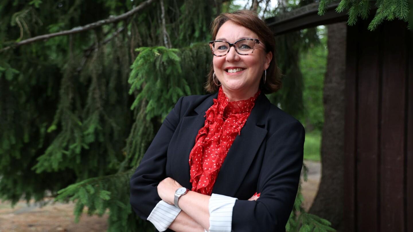 Lea Pääkkönen seisoo hymyilevänä suuren kuusen juurella.